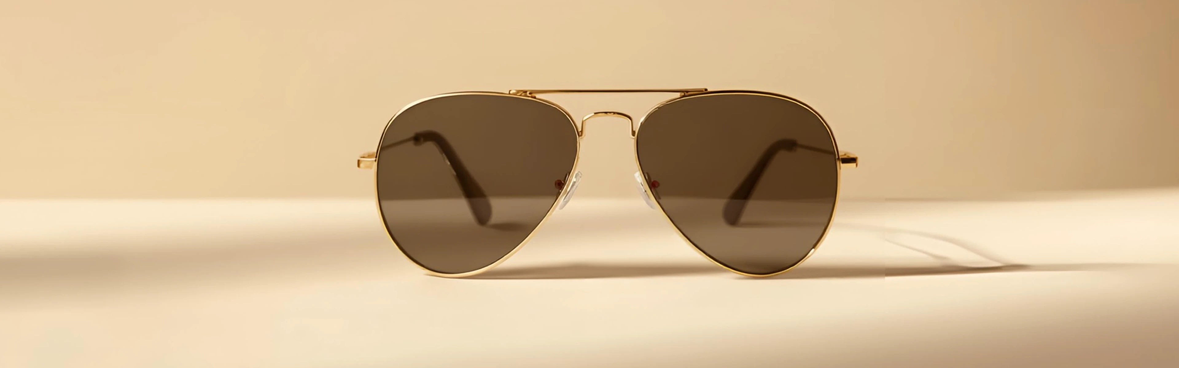 Gafas de sol de aviador con montura dorada y lentes oscuras sobre fondo beige.
